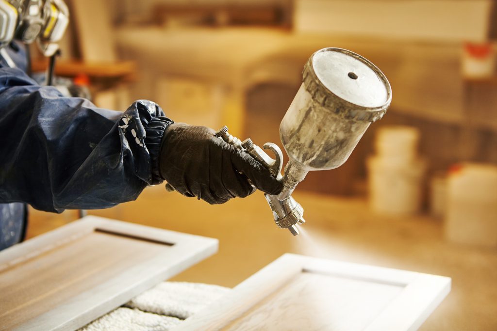 painter spraying paint on cabinet doors