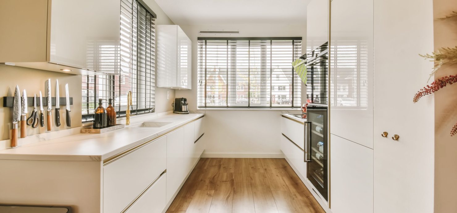 a kitchen with white cabinets and wood flooring in the middle of the room, looking towards the dining area