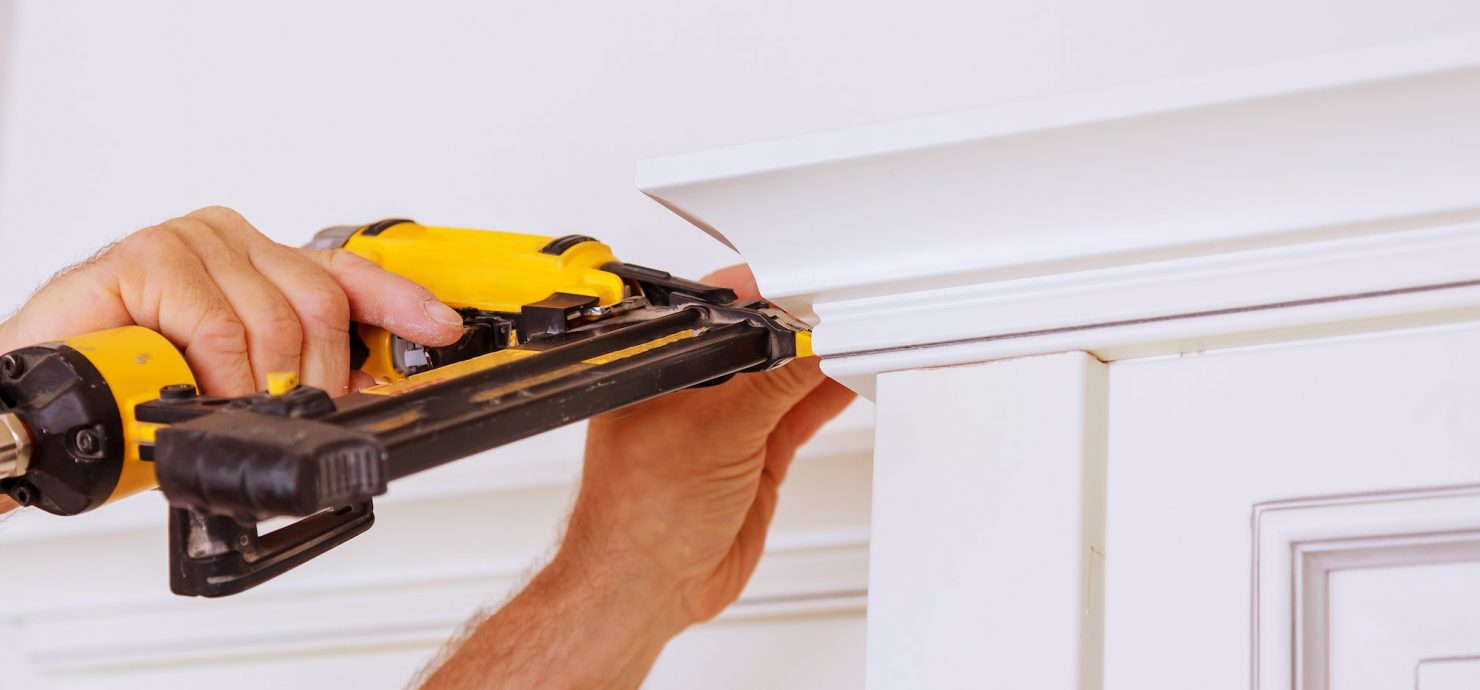 Carpenter brad using nail gun to Crown Moulding on kitchen cabinets framing trim