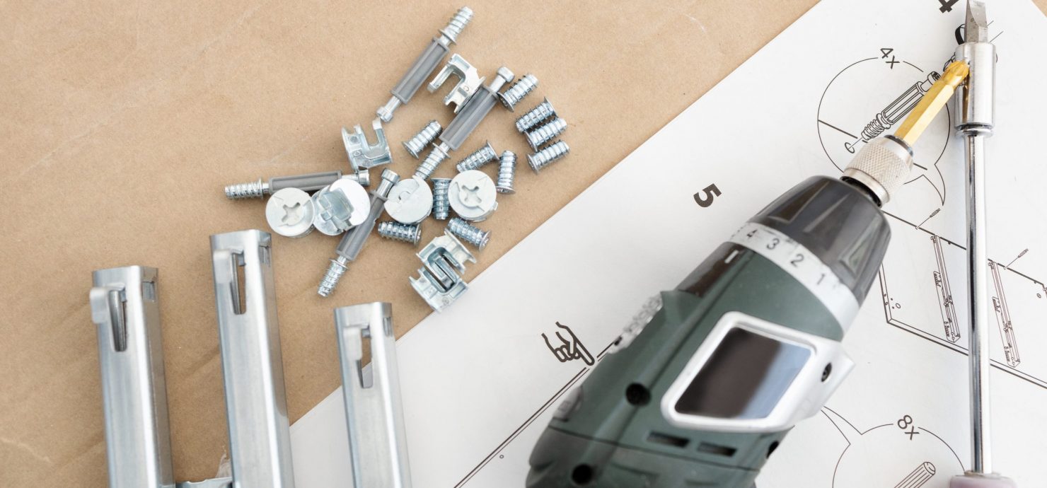 Top view of a cordless screwdriver, drawer sliders, screws and accessories. Assembling furniture concept. Copy space