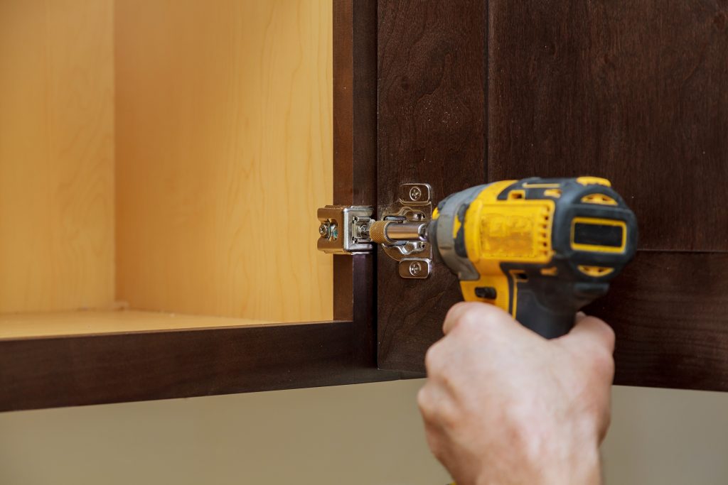 Installation of kitchen. Workman fixes a hinge to a kitchen cabinet.